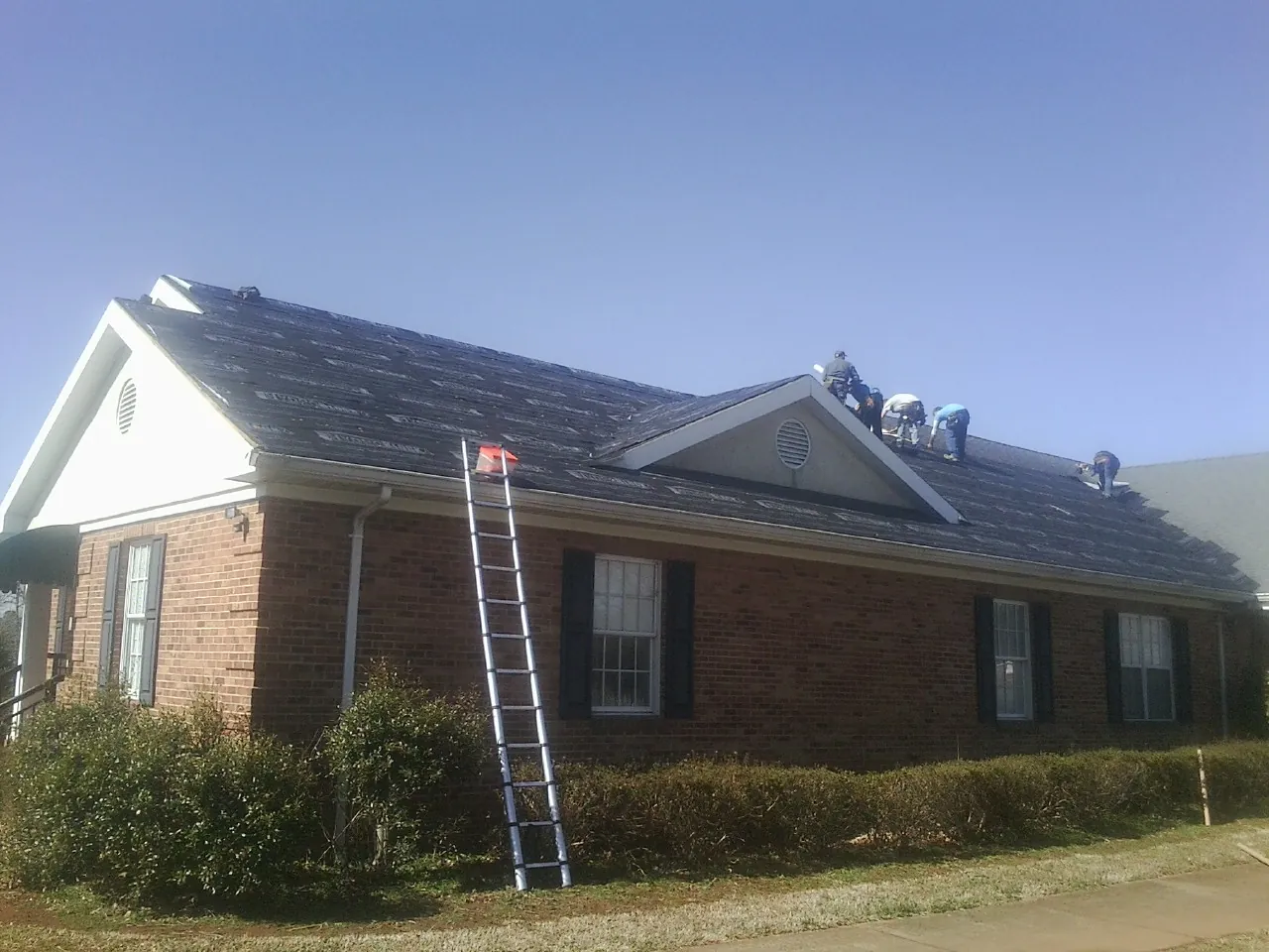 Crew tearing shingles off a brick ranch roof with a ladder set — Emergency Roof Repair work by our crew in Flomaton