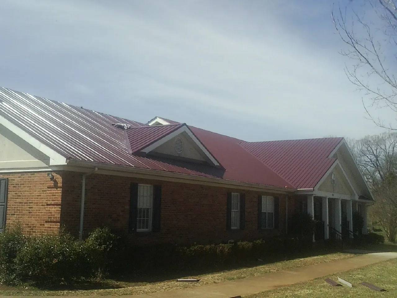 Red metal roof with gabled entries on a long brick building, from a Hail Damage Roof Repair job in Flomaton