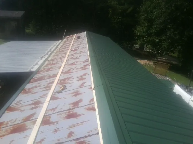Old rusted panels beside newly installed green metal roofing — Wind Damage Roof Repair by Roofing Brothers in Flomaton