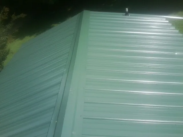 New green metal panels meeting at the ridge of a roof — Flat Roof Repair work by our crew in Flomaton