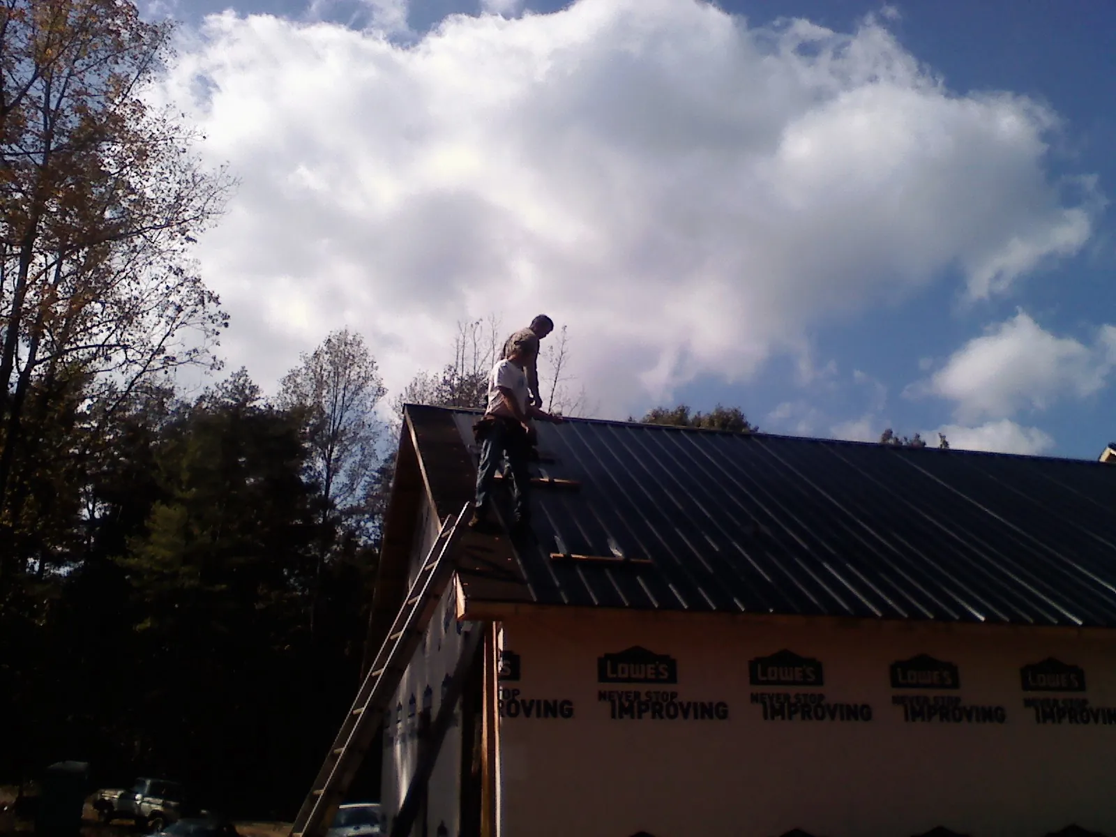Roofer fastening dark metal panels high against a cloudy sky, from a Roof Inspection job in Flomaton